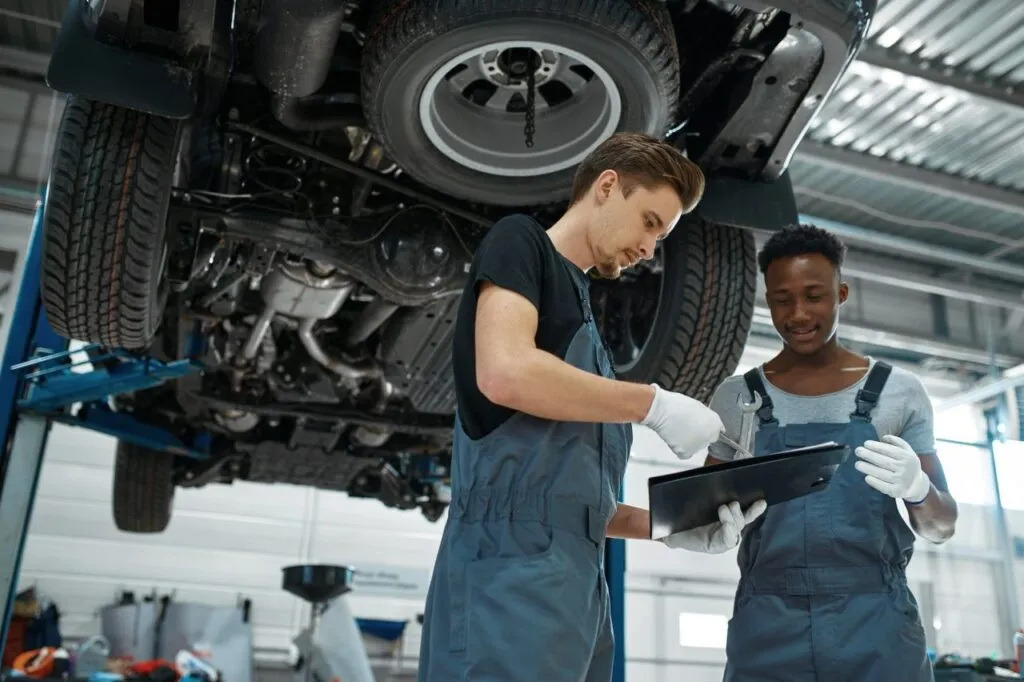 Two mechanics checking a service checklist under a car on a lift